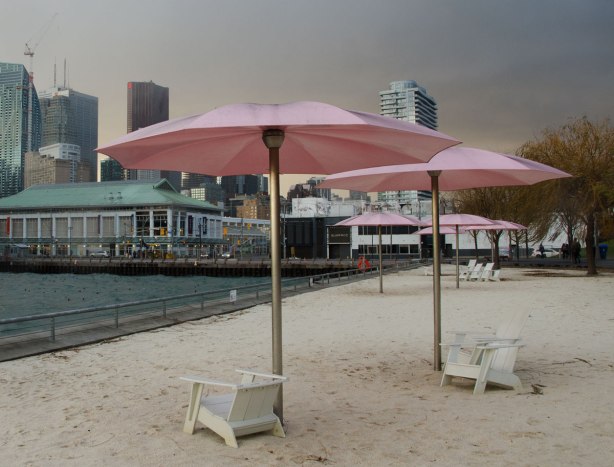 Sugar beach with its white chairs and pink umbrellas is in the foreground and the city is behind it.