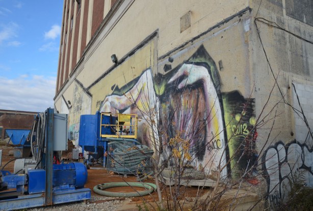 graffiti on the back of the Tower Automotive building, a tall brick building - looking along the side of the building, the head of the reclining woman is in the foreground.  Construction equipment is also in the picture. 