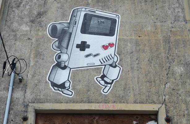 a large gameboy lovebot on the side of a concrete wall. 