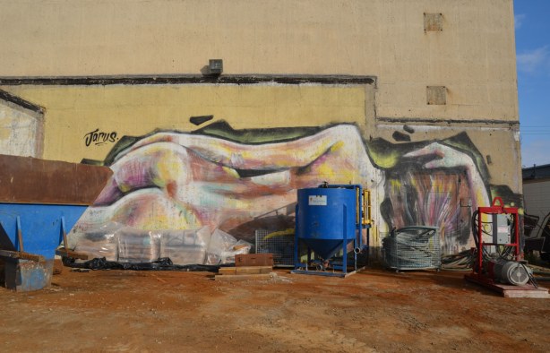 graffiti on the back of the Tower Automotive building, a tall brick building - the backside of a naked woman who is lying on the ground.  Much larger than lifesize, painted by Jarus. 