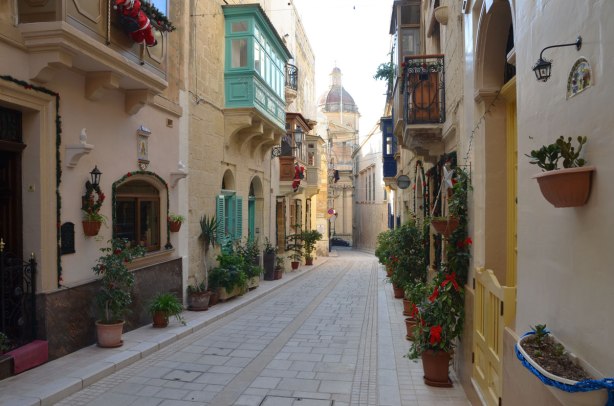 narrow street in Birgu, limestone buildings on both sides, colourful balconies overlooking the streets.