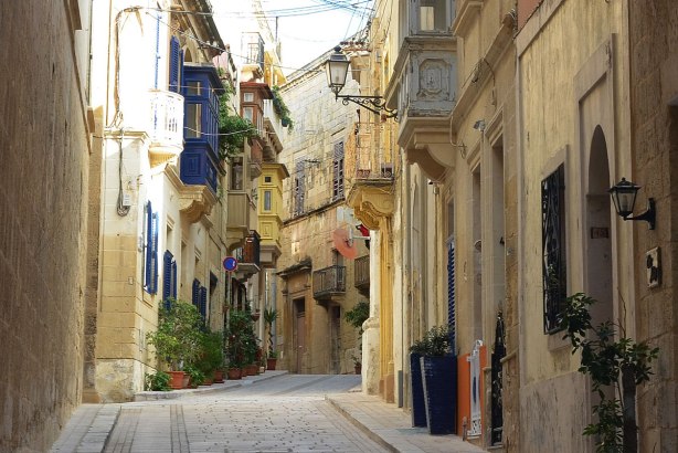 narrow street in Birgu, limestone buildings on both sides, colourful balconies overlooking the streets.