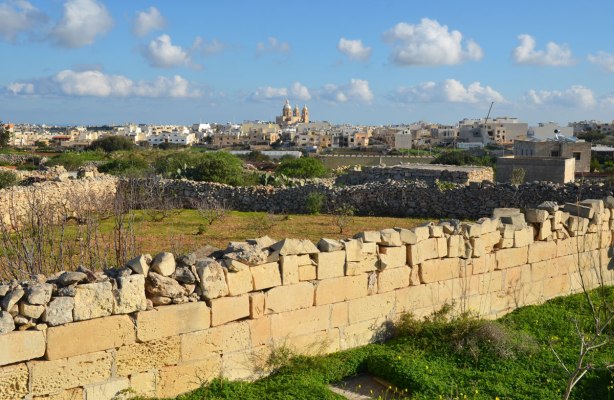 Looking beyond a low stone fence, past small fields surrounded by stone fences, to a city in the background with the steeples of a church clearly visible.