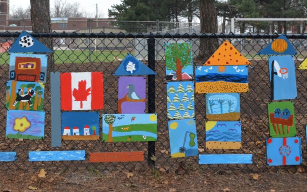 more of the collection of paintings by elementary school students that are hanging on a fence around the school. 