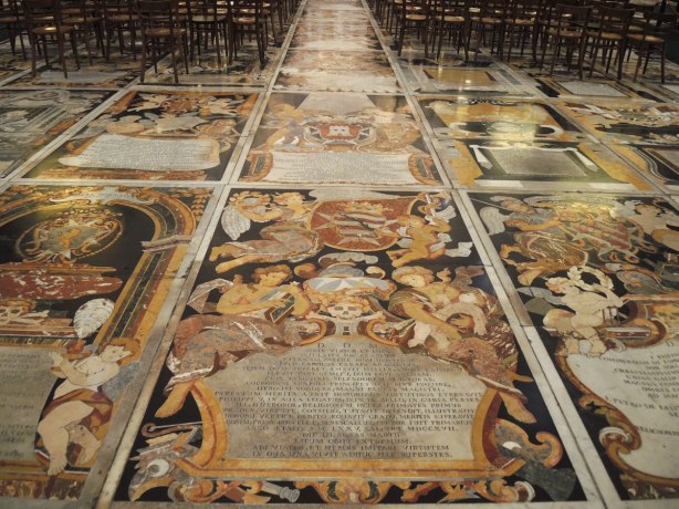 black, white, orange, gold tiles form memorials in the floor of St. Johns Co Cathedral in Valletta Malta. There are numerous angels, skulls and skeleton motifs that cover almost every inch of the cathedral floor.