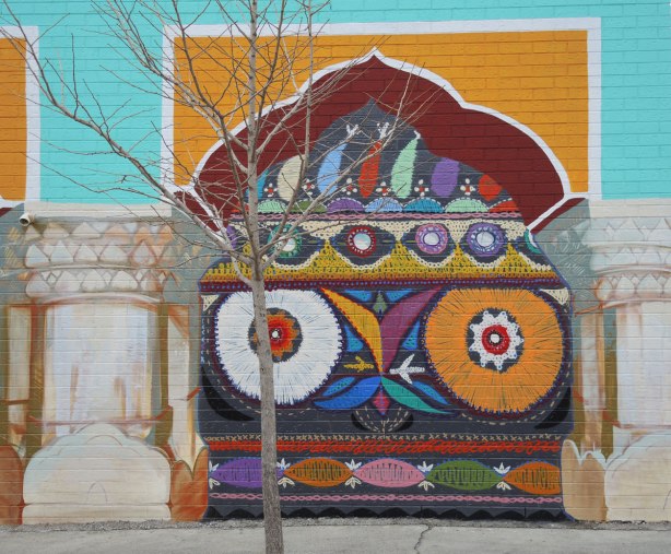 part of a mural, one of four panels painted to look like a yellow and red arch. under the arch is a bright multicoloured pattern reminiscent of South Asian fabrics and embroidery