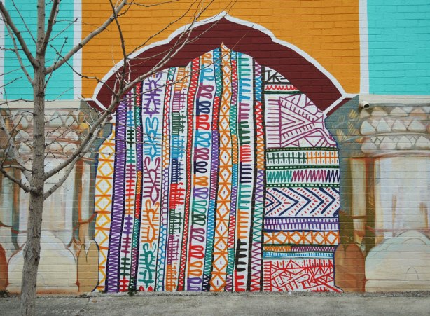 part of a mural, one of four panels painted to look like a yellow and red arch. under the arch is a bright multicoloured pattern reminiscent of South Asian fabrics and embroidery