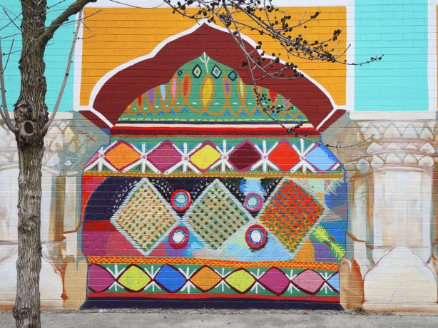part of a mural, one of four panels painted to look like a yellow and red arch. under the arch is a bright multicoloured pattern reminiscent of South Asian fabrics and embroidery