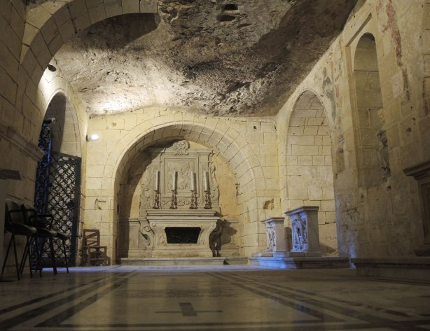 Inside St. Pauls grotto, an altar with candlesticks against the far wall, tile floor with memorials to the people buried underneath, the ceiling is natural rock.