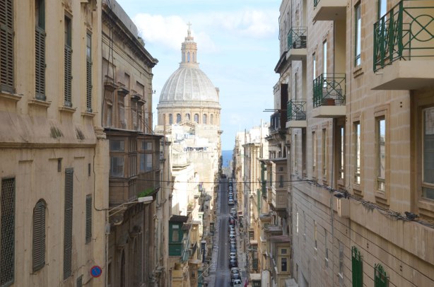 looking down a street that goes downhill, buildings on either side, a large round church dome in the distance.