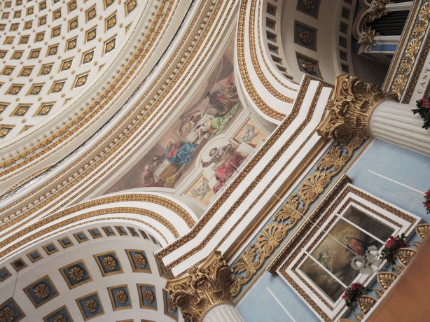 interior of a church showing a small part of the domed ceiling, part of two supporting arches and the picture that is painted in the space between the adjoining round arches.