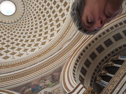 looking towards a large domed ceiling of a church with one of the rounded supporting arches in view. part of my face is also in the photo.