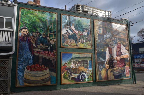mural in 4 parts, 1 on the left, 1 on the right and 2 in the center.  The left depicts a man selling apples, the right depicts a cobbler fixing shoes.  In the center: bottom, a family in old fashioned car.  Center top - a family sitting in a livingroom including a man in a rocking chair 