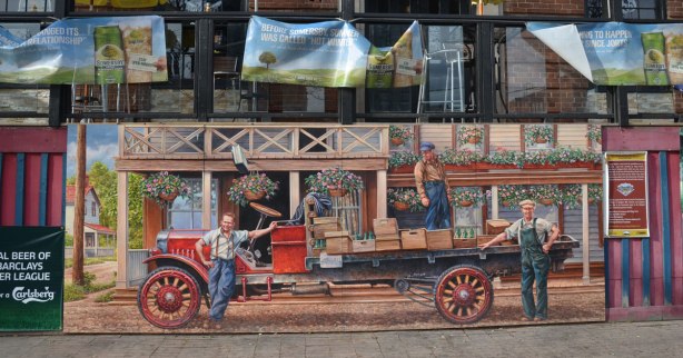 mural showing men loading an old flat bed truck with crates of empty pop bottles, 1920s