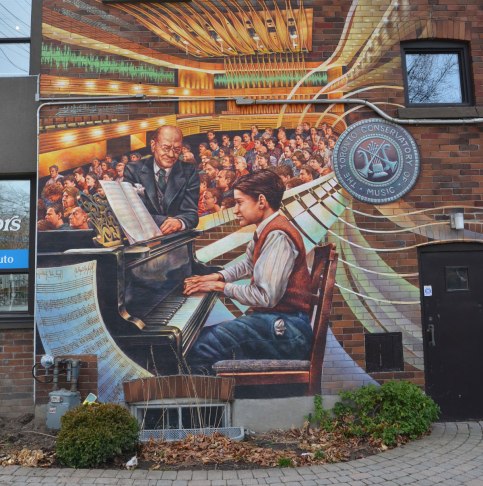 mural depicting a boy playing a piano in front of an audience.  A man is helping to turn the pages of the music. 