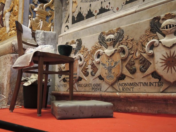 A chair is beside an ornately decorated wall. It is there for the person who is doing restoration work on the wall.