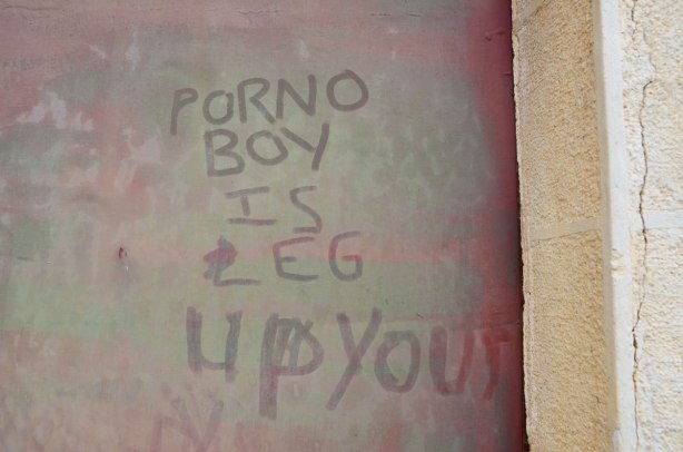 A dirty window on which someone has written the words 'porno boy is leg up you' in the dirt.