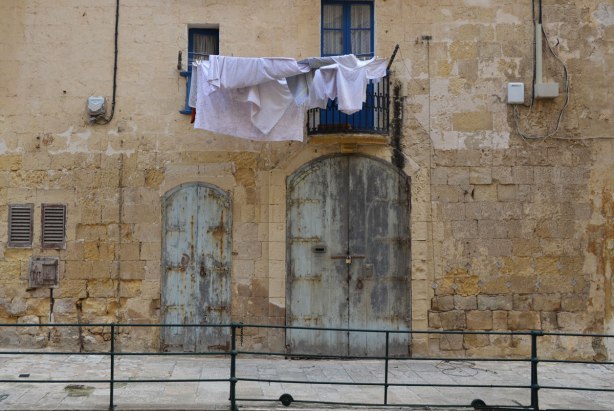 Laundry hanging from a balcony in Valletta Malta, limestone buildings and wooden shuttered doors