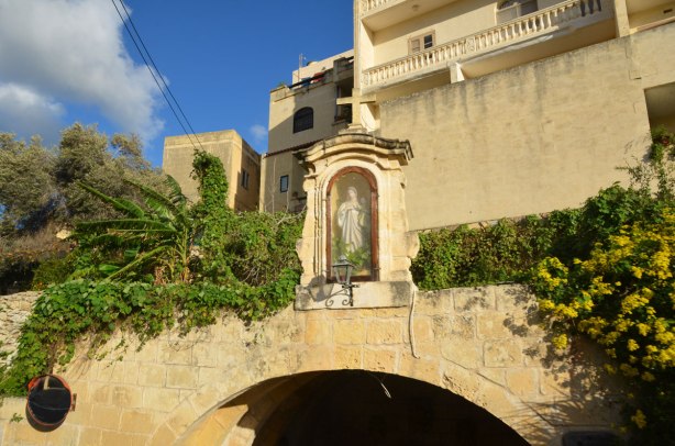 The top part of a rounded stone arch with a stone case with a Mary statue in it. The case has a glass front.