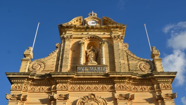 The top part of the front of a limestone church with a statue of Mary in a niche.