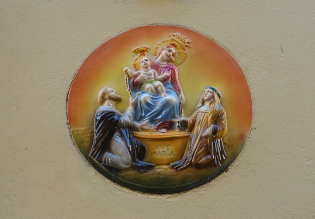 A round medallion of Mary holding the baby Jesus on a raised surface. Two men are kneeling below and looking up towards mother and child