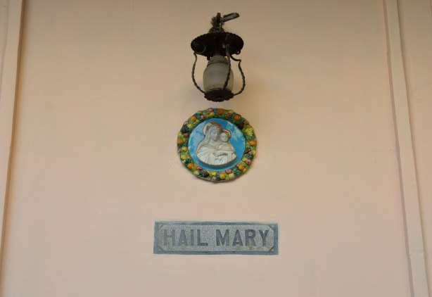 A round medallion of Mary and the baby Jesus, with the words 'Hail Mary' in grey beneath. A light is above the medallion.