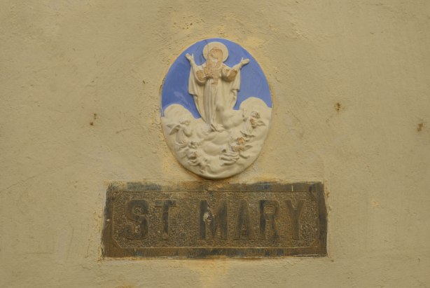 A blue and white oval shaped medallion of Mary standing on a cloud. The words 'St. Mary' are in brown underneath.