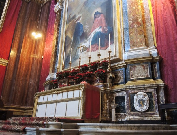 altar with tall candles and poinsettias for Christmas. A large religious painting is above the altar.