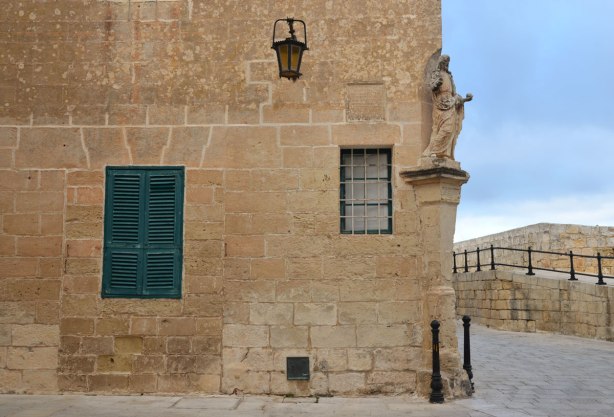 Small stone religious statue on the corner of a limestone building.