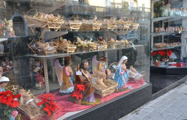 Religious figurines in a shop window. Most are for Christmas nativity scenes. There are a lot of baby Jesus's in straw filled wooden managers.