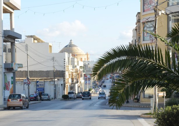looking down a street, palm tree, buildings, cars, and the dome of a large church at the bottom of the street