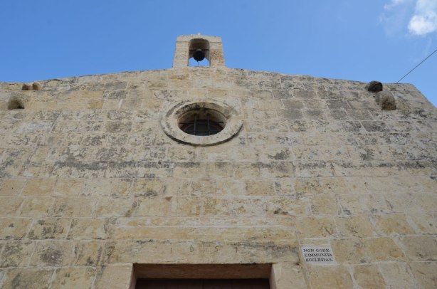 top of the front part of an old church.  It has a  small round window.  The number 1657 is carved into the stone over the doorway.  