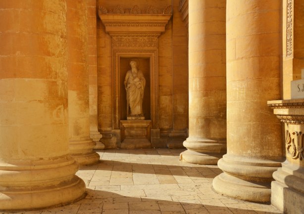 A statue of a saint, St. Simon is a niche in the background. the base and lower part of of four large columns is in the foreground.