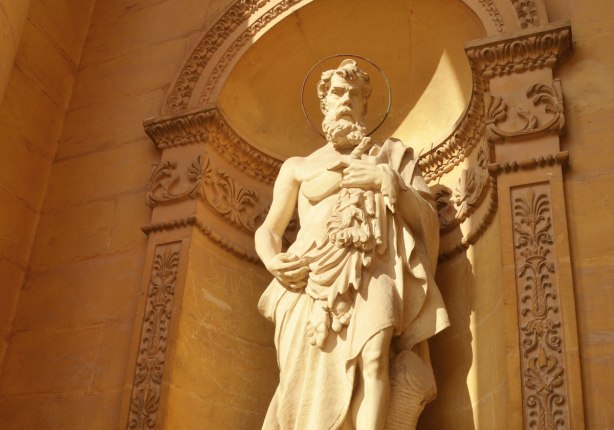 Top part of a statue of St. Bartholomew made of limestone in a niche with a rounded top.