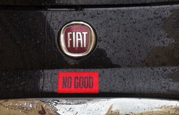 The back part of a black Fiat 500 on which someone has added a red sticker that says NO GOOD