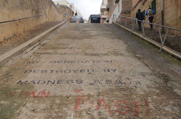 Street, going up a steep hill, on which someone has printed, in large black block letters, a line from 'Howl' a poem by Allen Ginsberg