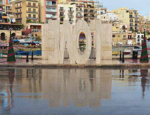 The LOVE sculpture beside the road, block letters inverted. When they are reflected in the wet pavement, the word is no longer upside down, but it is still backwards.