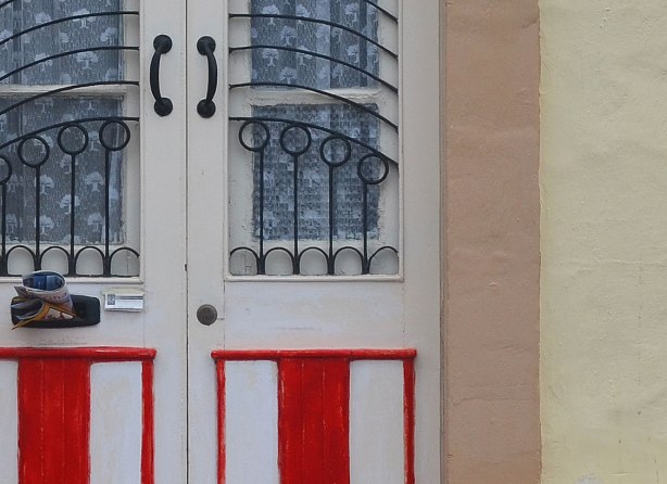 close up of a door. The lower part is painted in red and white stripes. The upper part has two glass panels that are covered in interesting metal bars that are curved and circular