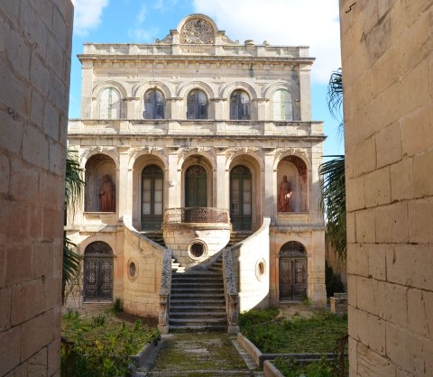an old, large, ornate, 3 storey abandoned stone house in Rabat with grass growing over the stone path to the entrance