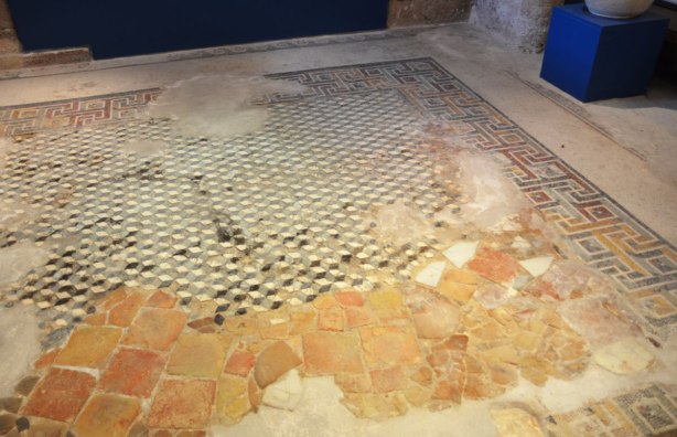 Roman mosiac floor in various states of repair. Some smaller tiles and some medium sized tiles.