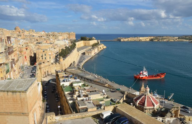 shoreline of Valletta, with blue water, limestone walls, limestone buildings and a blue sky.