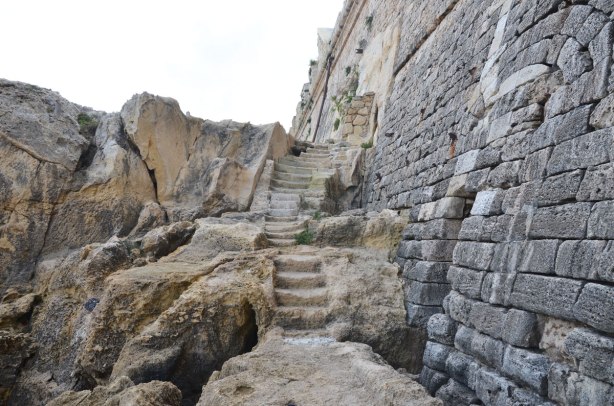 Steps carved into the rocks at the base of a stone wall.