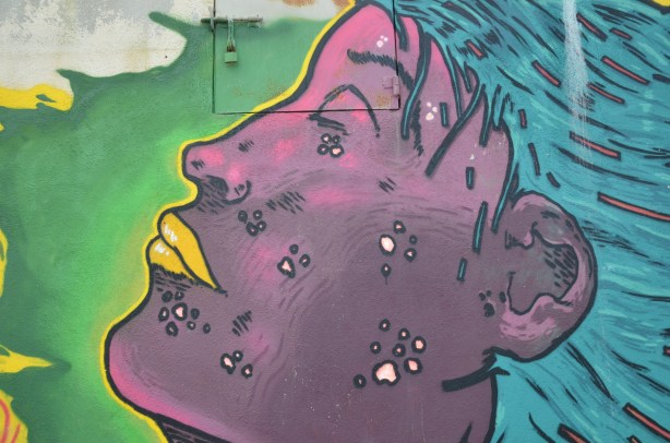 Street art painting of a large purple face in profile. Yellow lips, blue hair.