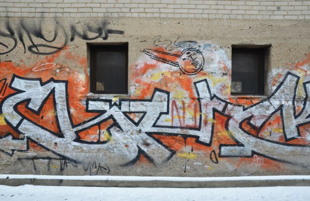 tags on a brick wall in black, orange and white.  Anti Rob Ford graffiti also there in the form of a crack pipe with Fords face on it.  "Spud doesn't condone crack"  I think are the words written beside the crack pipe. 