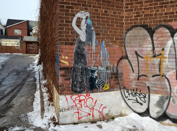 Wheatpaste paste up picture of a woman in a long black sleeveless dress who is pouring water from a jug over the back of her head.   The water is falling on a girl who is sitting behind the woman.  The girl is holding an umbrella. 