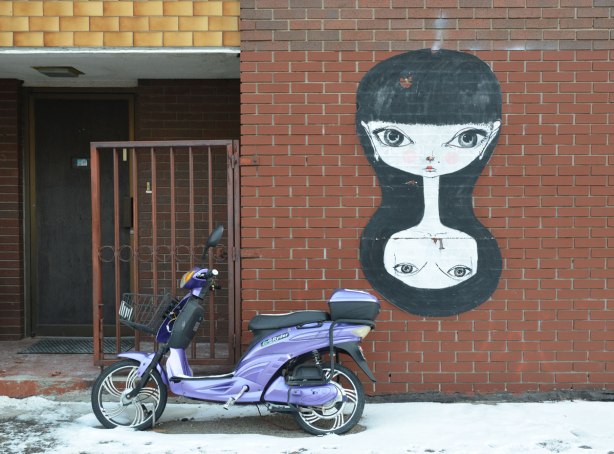 A wheatpaste paper graffiti piece of a girl's head in duplicate, looks like she's reflected below. Long black hair. Big black eyes.