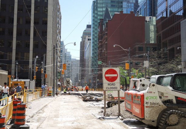 a section of city street is being renovated.  The pavement has been removed, construction equipment and vehicles are in the picture.  There is a 'road closed' sign. 
