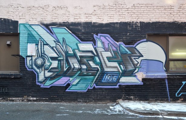 HUG graffiti tag and drawing in blues, greys and purples on a black and white wall.