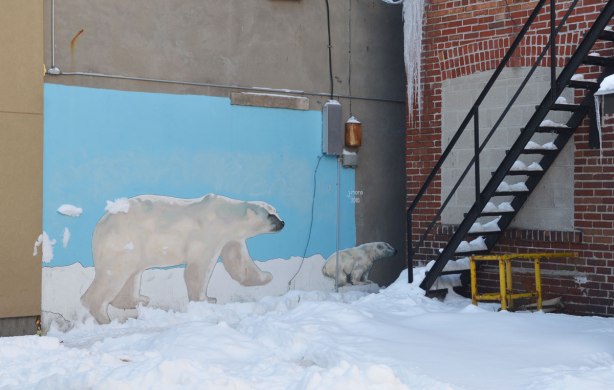 A mural on a wall of two polar bears - an adult and a young cub.  It looks like they are walking on the snow. 