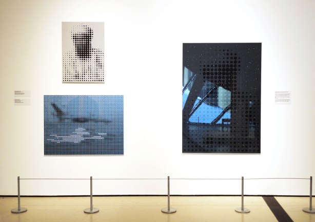 three paintings hanging on a wall in an art exhibit.  One is of Osama bin Laden and the other two are 9/11 related, New York .  